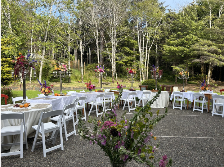 Whimsical forest reception setup with bright florals and round tables surrounded by towering evergreens.